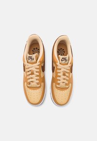 Narancssárga és bézs bőrből készült Nike Air Force 1 sportcipők. Bézs fűzőkkel, barna velúrvágott logóval, perforált orral és mintázott talpbetéttel rendelkeznek.