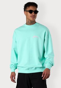Mint green sweatshirt in cotton blend, features a crew neckline, ribbed cuffs, and small pink embroidered logo on the left chest.