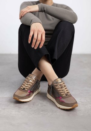Zapatillas marrones y grises con un acabado texturizado, detalles en cuero, un toque de color rosa y cremallera lateral. Suela de goma, silueta moderna.