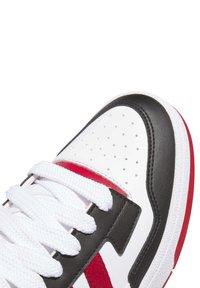 Primo piano della punta di una sneaker bianca, nera e rossa con lacci bianchi e dettagli traforati sulla tomaia in pelle bianca.