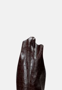 Borsa in pelle borchiata con stampa coccodrillo, di un elegante bordeaux scuro, dal design sleek e minimalista e con una forma arrotondata nella parte superiore. Dettaglio con zip su un lato.