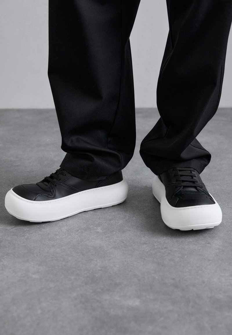 Zwarte leren sneakers met een witte plateauzool. Kenmerken zijn onder andere veters, een ronde neus en subtiele stikdetails. Geschikt voor casual gebruik.