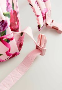 Zaino rosa con motivo floreale e superficie texturizzata, dotato di manici rosa e fibbie in plastica. Cinghia etichettata "BAKER" con lettering in rilievo.