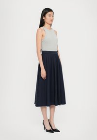 Grauer ärmelloser Top kombiniert mit einem marineblauen gefältelten Rock, der subtile vertikale Streifen hat, sowie schwarzen spitzen High Heels für einen ausgewogenen Look.
