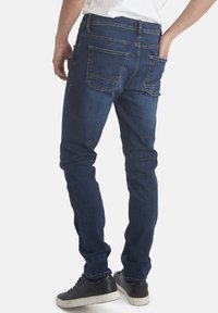 Mörkblå denimjeans med slim fit, med två bakfickor som har kantiga sömmar och en subtil textur. Bärs med svarta sneakers.