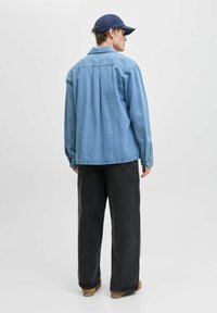 Lichtblauw denim shirt met lange mouwen, rugpas en knopenmanchetten, gecombineerd met losse zwarte jeans en een marineblauwe pet.