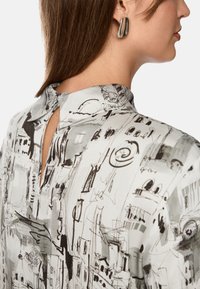 Bluse mit Kragen aus leichtem Stoff, die mit einem schwarz-weißen abstrakten Stadtbilddruck versehen ist. Mit einem Schlüsselaugen-Detail am Rücken und einer glatten Textur.