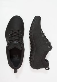 Scarpe sportive nere realizzate in materiali sintetici con una tomaia texturizzata, chiusura con lacci, colletto imbottito e suola in gomma con motivo a rilievo.
