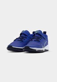 Zapatillas deportivas azules con diseño de malla, punta redonda, correa ajustable y suela texturizada. Presenta detalles en verde y una entresuela blanca.