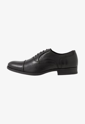 Chaussure habillée pour homme en cuir noir avec laçage fermé et petit talon, présentée de profil sur fond blanc.
