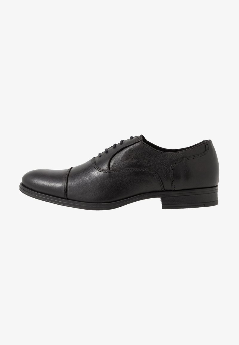 Chaussure habillée pour homme en cuir noir avec laçage fermé et petit talon, présentée de profil sur fond blanc.