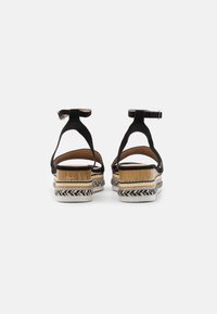 Sandali neri in suede con cinturini alla caviglia, suole a piattaforma con texture intrecciata e dettagli a strati in marrone, bianco e nero.