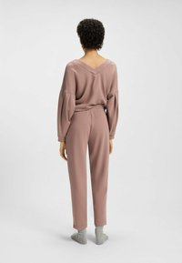 Losse loungewearset in zachte, gedempte rozenstof; het pullover heeft een diepe V-hals aan de achterkant en de taps toelopende broek heeft een elastische tailleband.