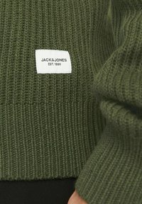 Olivově zelený pletený svetr s žebrovanou strukturou a bílou nálepkou s nápisem "JACK & JONES EST. 1990" na přední straně.