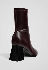 Burgundy nahkasaappaat nilkkapituisuudella, jossa on tyylikäs muotoilu, nelikulmainen musta korko ja kontrastivärinen vaaleanpunainen ommel sauman kohdalla. Tyylikäs, kiiltävä pinta.