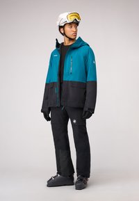 Zweiteiliges Winter-Ski-Outfit bestehend aus einer wasserfesten Jacke in Türkis und Schwarz mit Kapuze sowie schwarzen isolierten Hosen. Enthält Handschuhe und Skischuhe.