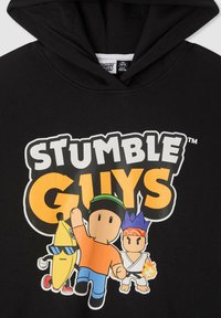 Felpa nera con cappuccio caratterizzata dal testo "Stumble Guys" e tre personaggi cartoon: una banana con occhiali da sole, una persona vestita di arancione e un combattente avvolto nel fuoco.