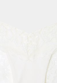 Vêtement blanc avec un col en V en dentelle. Dentelle texturée superposée sur un tissu doux, avec des motifs floraux et des bords festonnés.