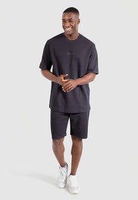 T-shirt noir à manches courtes et short assorti en tissu lisse et respirant. Le t-shirt présente un logo discret. Porté avec des baskets blanches.