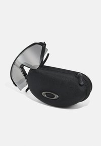 Ochelari de soare sport negri cu lentile gri, având un design ajurat, așezați pe un etui texturat negru cu fermoar care afișează un logo oval.