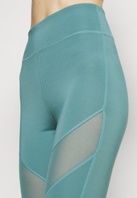 Leggings en tono aguamarina con una cinturilla alta y cortes de malla a los lados, con costuras planas para mayor comodidad y flexibilidad.
