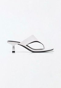 Hvid læder-sandal med hæl, thong-strop, firkantet tå og lav kittenhæl på hvid baggrund.