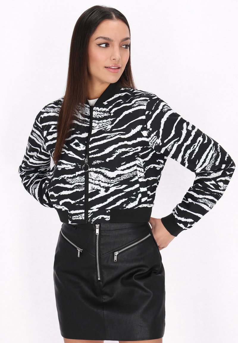 Chaqueta bomber a rayas de cebra en blanco y negro con cierre de cremallera, puños acanalados y diseño ajustado, combinada con una minifalda de cuero negra con cremalleras.