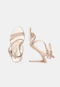 Sandaletter med høje hæle i blød beige med en glitrende finish, med to smalle stropper og guld-tone spænde accenter.