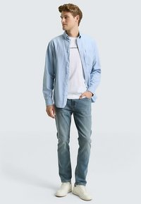 Jasnoniebieska koszula zapinana na guziki, biała koszulka pod spodem, niebieskie dżinsy i białe trampki. Luźny krój, gładka tkanina i swobodny styl.