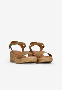 Sandalias de cuña de ante marrón con dos correas cruzadas y una correa en el tobillo, que presentan una apariencia de madera clara texturizada en la suela de la cuña.