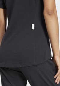 T-shirt noir avec une couture horizontale, texture douce et une petite étiquette blanche avec "A TERRY" sur le côté. Porté avec un pantalon assorti.