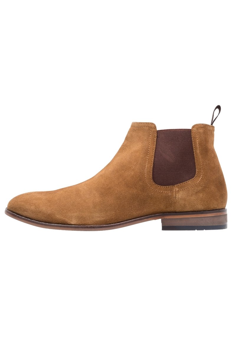Stivale Chelsea da uomo in suede marrone con pannello elastico laterale e tacco basso impilato, mostrato dal lato esterno su sfondo bianco.