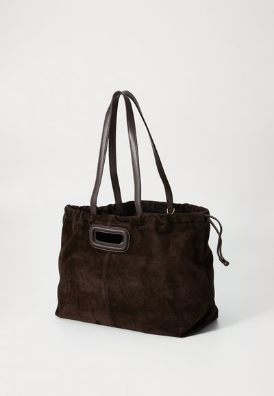 Brown suede tote bag with a gathered top and dark leather handles, featuring an oval cutout detail on the front. Smooth texture.