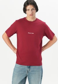 Rode T-shirt van katoen met een ronde halslijn en korte mouwen. Een klein wit tekstlogo is gecentreerd op de borst. Draag het met lichtblauwe jeans.