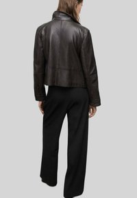 Brązowa skórzana kurtka o skróconym fasonie, z dopasowanym kołnierzem i widocznym przeszyciem. Noszona z długimi czarnymi spodniami, podkreślająca smukłą sylwetkę.