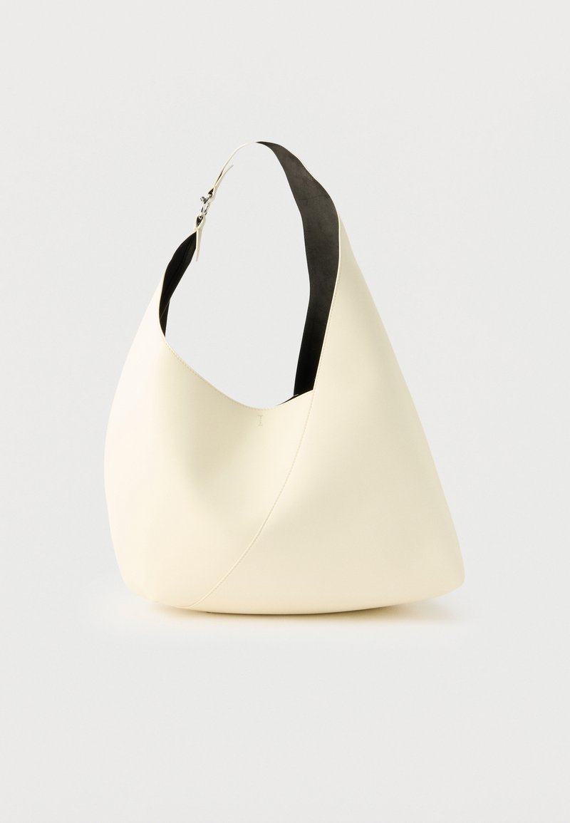 Sac bandoulière en cuir couleur crème avec une large sangle et une boucle argentée sur un fond blanc uni.