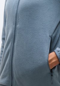 Φλις μπουφάν σε απαλό μπλε, με μπροστινό φερμουάρ, πλαϊνές τσέπες με κλείσιμο φερμουάρ και απαλό υφή.