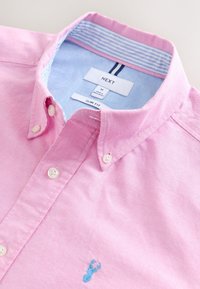 Light pink slim fit shirt with white buttons, featuring a blue embroidered deer logo and a light blue striped inner collar.