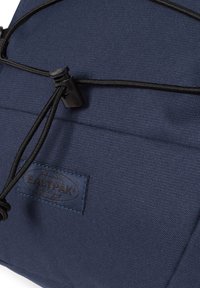 Mochila azul marino hecha de tela duradera, con una superficie texturizada, un cordón negro ajustable y una etiqueta con el logotipo de Eastpak en relieve.
