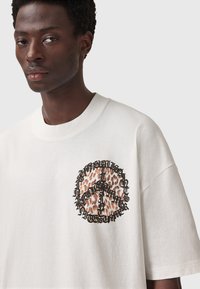 Hvid oversized t-shirt med en rund leopardprint og sort grafisk tekstdesign på brystet. Lavet af bomuldsmateriale med blød tekstur.