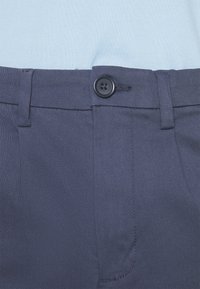 Mörkblå byxor i slätt tyg, med knappstängning fram, bältes-loopar och sidofickor med skräddarsydd design.