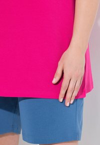Top fucsia a maniche corte con orlo arrotondato e pantaloni blu. Il tessuto sembra morbido, con cuciture visibili e una texture liscia.