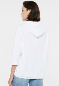 Weiß gestreifter Hoodie mit einer Fronttasche, kurzen Ärmeln und einer Kordelzugkapuze, kombiniert mit hellblauen Jeans.