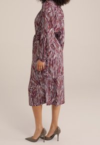 Long, purple dress featuring a colorful abstract pattern. Made of lightweight fabric with long sleeves and a belted waist. Worn with grey heels.
