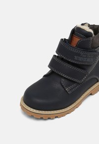 Botte pour enfants en cuir bleu marine avec double bande Velcro, semelle en caoutchouc marron clair et doublure intérieure douce.