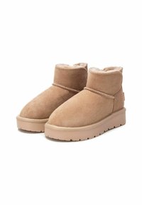 Botas de tobillo de ante beige con forro de pelaje sintético, punta redondeada y suela de goma. Diseño de perfil bajo con un detalle de costura sutil.