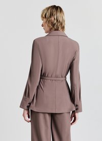 Brown tailored jacket with a belted waist, long sleeves, and buttoned cuffs. Smooth fabric and structured design, seen from the back.