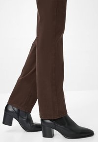 Bottines noires à talon avec une texture lisse, bout pointu et talon épais, associées à un pantalon droit marron.