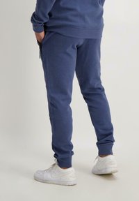 Marineblauwe joggingbroek van zachte stof, met een taps toelopende pasvorm en elastische boorden. Gecombineerd met witte sportsneakers.