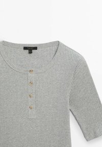 Haut en maille côtelée gris clair avec encolure ronde, manches courtes et quatre petits boutons beiges sur la patte de boutonnage devant.